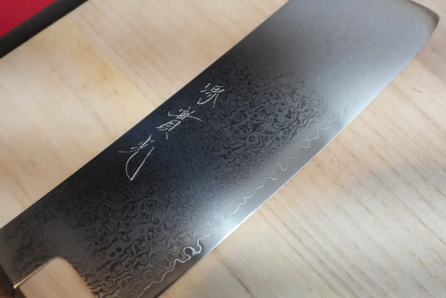 Hand-forged Damascus nakiri blade with engraved kanji, photographed in low light